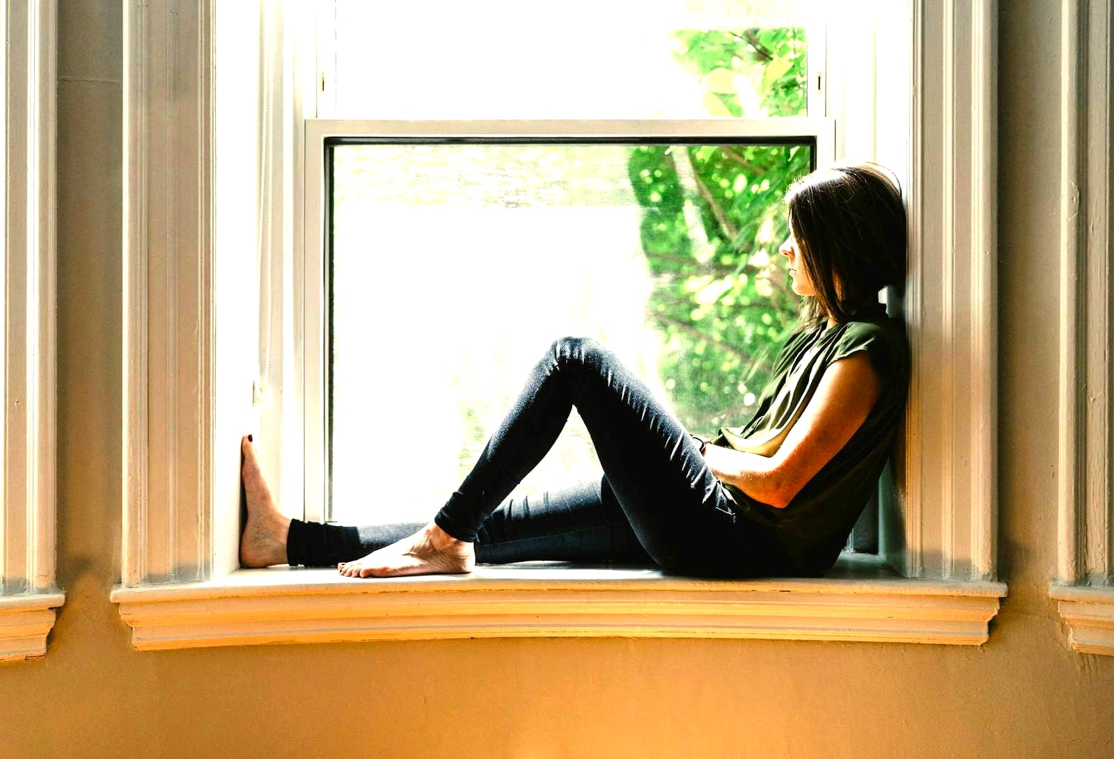 A young person sitting in a window recess in daylight